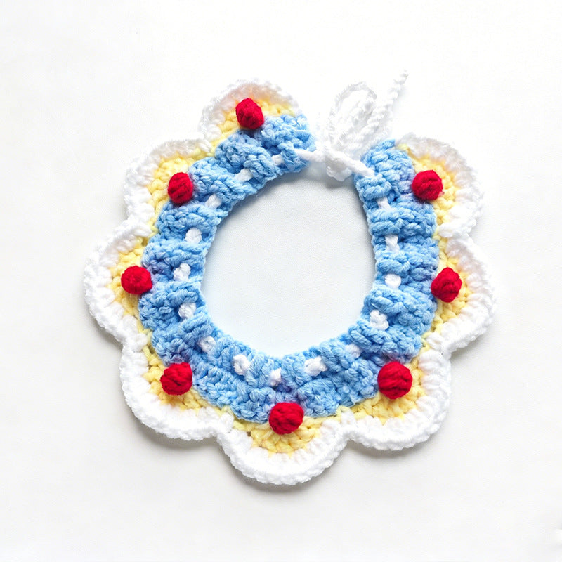 Handmade crochet pet collar in blue and yellow with red pom-poms, flat lay \| Knoblom