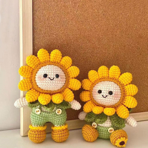Two crochet sunflower dolls leaning against a wooden picture frame